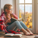 girl sitting in window reading book